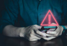 Beloved Mascot Stops Laughing – Why Now? Person holding phone with warning symbol displayed.