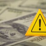 NEWS ALERT: $120 Warning Issued A yellow warning sign placed on a background of dollar bills