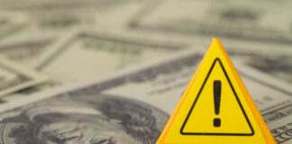 A yellow warning sign placed on a background of dollar bills