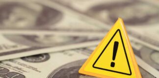A yellow warning sign on a background of dollar bills