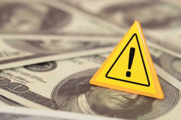 The,Cautionary,Triangle,Sign,Amidst,A,Sea,Of,Dollar,Bills A yellow warning sign on a background of dollar bills