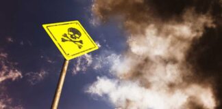 Yellow skull and crossbones warning sign against smoky sky