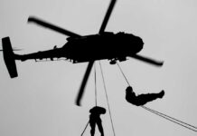 Silhouette of a helicopter with two individuals being lowered by ropes