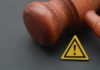 Wife’s Cliff Ordeal – Judge Drops Bombshell Wooden gavel with a yellow warning triangle sign on dark surface