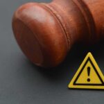 Wife’s Cliff Ordeal – Judge Drops Bombshell Wooden gavel with a yellow warning triangle sign on dark surface