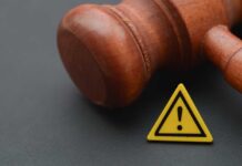 Wooden gavel with a yellow warning triangle sign on dark surface