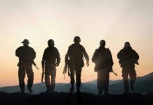 Pentagon Orders Annual T Tests — NEW DETAILS Five armed soldiers silhouetted against sunset background.