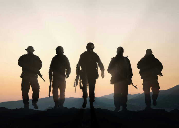 shutterstock_401342968 Five armed soldiers silhouetted against sunset background.