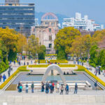 Visitors at Hiroshima Peace Memorial Park with cherry blossoms and memorial structures