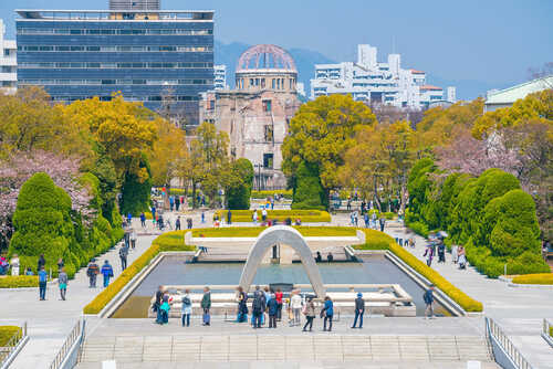 Visitors at Hiroshima Peace Memorial Park with cherry blossoms and memorial structures