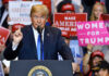 Donald Trump speaks at a rally with Bill Kenney in the crowd holding signs