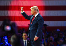 Donald Trump raises a fist on stage before a large U.S. flag
