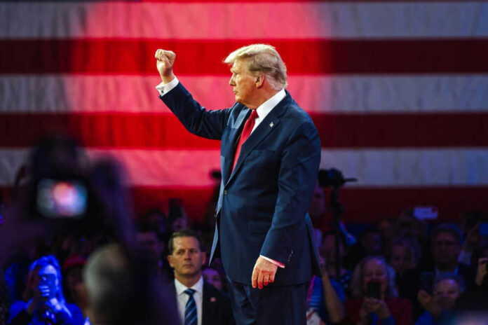 Donald Trump raises a fist on stage before a large U.S. flag