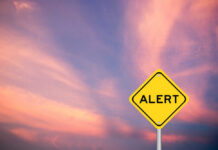Drone Attacks Trigger U.S. Pullback Yellow alert sign against a colorful sunset sky