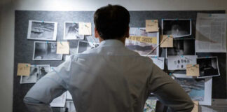 Man examining investigation board with photos and notes.