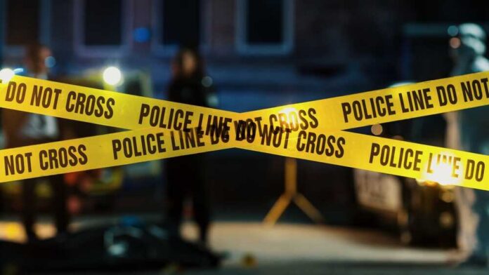 Police tape marking a crime scene with blurred figures in the background