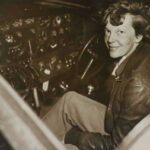 Amelia Earhart Clue Emerges Amelia Earhart seated in an airplane cockpit, looking toward the camera