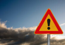 A triangular warning sign with an exclamation mark against a cloudy sky